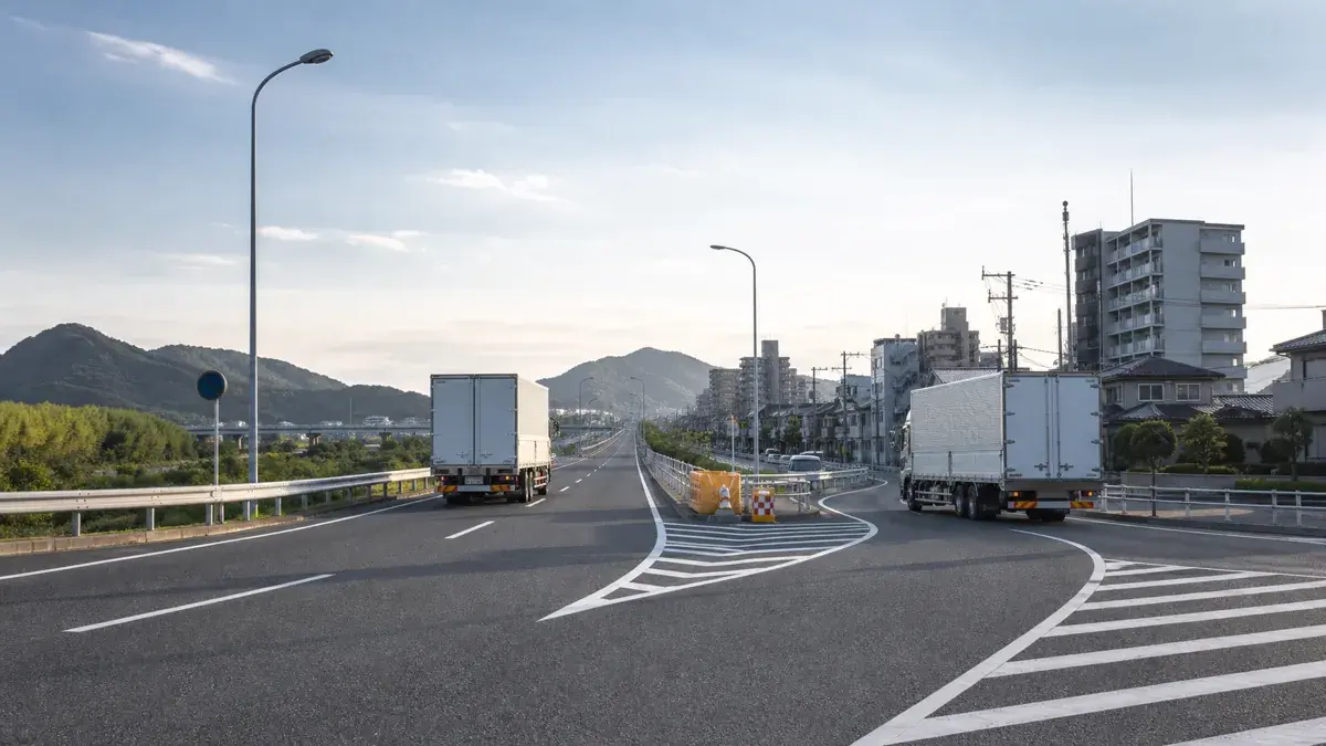 長い幹線道路と市街地の配送路へ分かれる分岐を走る二台のトラック